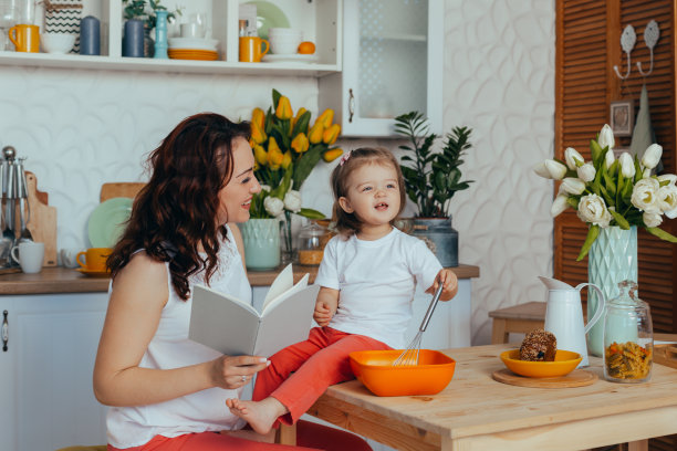 美丽的年轻妈妈和她可爱的小女儿在厨房做饭的时候玩耍和微笑。图片下载