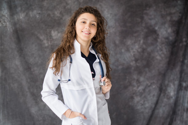 笑容满面的医生在白色制服站在灰色的背景。本空间图片下载