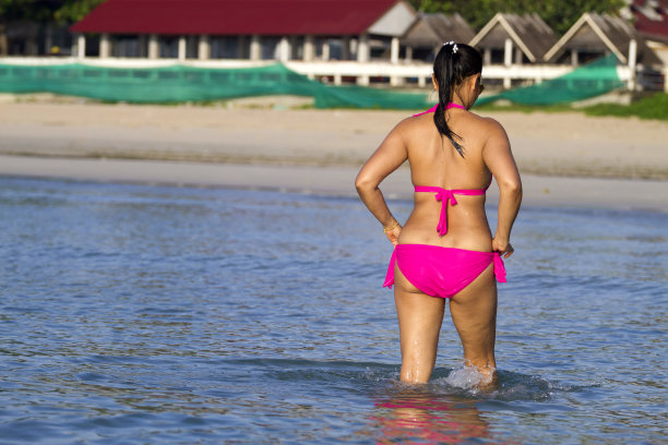 穿着粉红色比基尼的女人走在海滩上图片下载