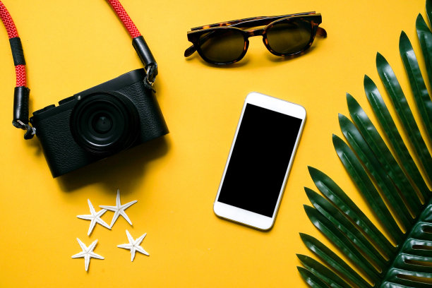 近距离俯瞰黑色相机，智能手机，太阳镜，海星和棕榈叶在黄色背景夏季旅游和时尚配饰概念图片下载
