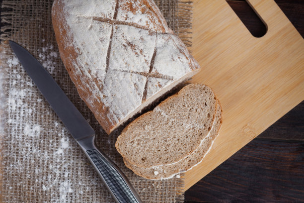 新鲜的黑面包片在橡木板上，撒上面粉，在亚麻织物的木制背景上，用钢刀。照片俯视图图片下载