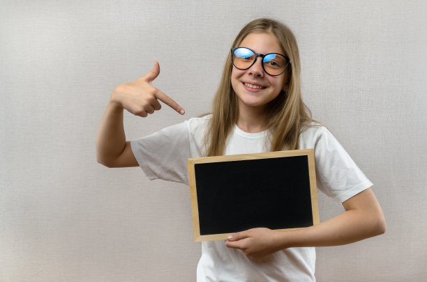 漂亮的淘气的小女孩，戴着眼镜，手里拿着一个牌子。copy-space。图片下载