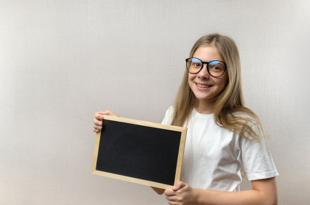 漂亮的淘气的小女孩，戴着眼镜，手里拿着一个牌子。copy-space。图片下载