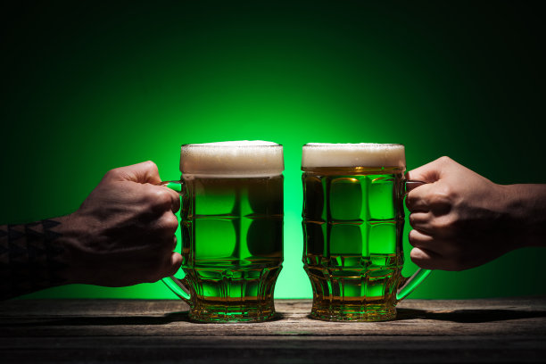 在绿色的背景上，男人拿着啤酒杯的裁剪视图图片下载