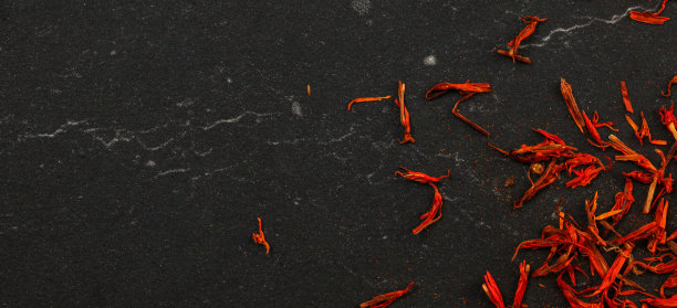 桌面照片，明亮的橙色红色，藏红花香料番红花花柱头和风格的螺纹黑色工作板与大理石图案，宽幅横幅空间文字留下图片下载
