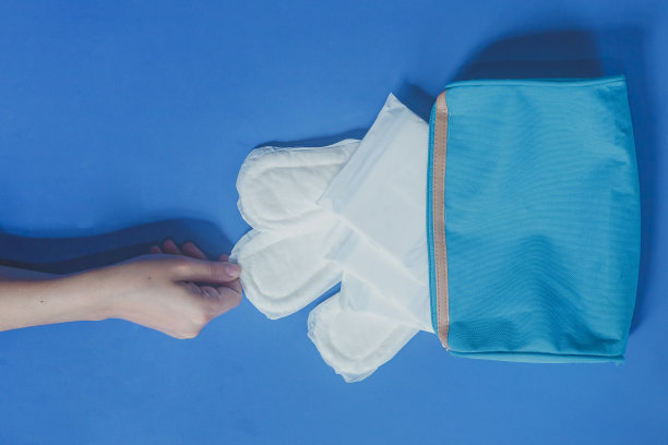 年轻女性把卫生巾放在她的化妆包的蓝色背景图片下载