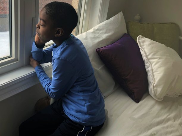 一个小男孩坐在床上望着窗外在一个阴沉的日子图片下载