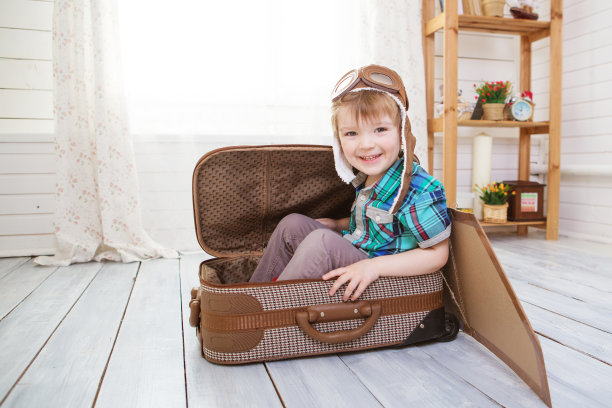 小男孩坐在手提箱上玩飞机模型。幻想旅行概念。图片下载