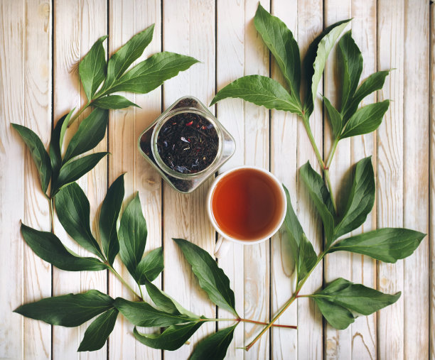 干红茶在玻璃罐和一杯茶在木背景牡丹绿叶。图片下载