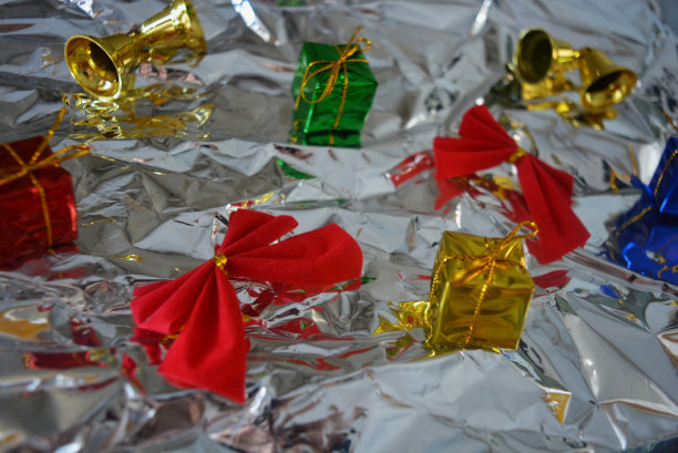 新年假期有红色的蝴蝶结和金色的铃铛，红色的蝴蝶结在光滑的铝，金属皱巴巴的纸上。图片下载