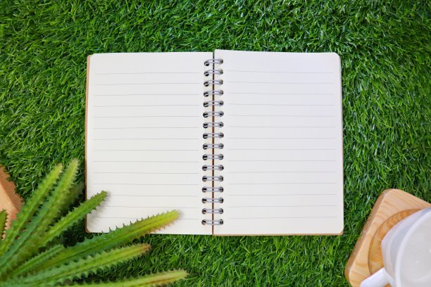 笔记本为写抄文本，纸张以绿草为背景图片下载