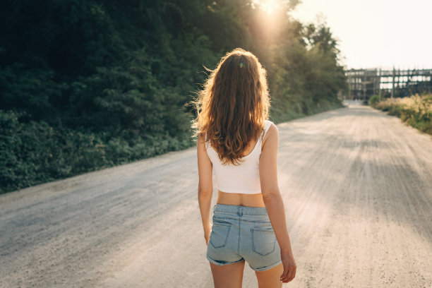 一个头发散乱、身材苗条的年轻女子在夏天的阳光直射下走在前面的路上图片下载