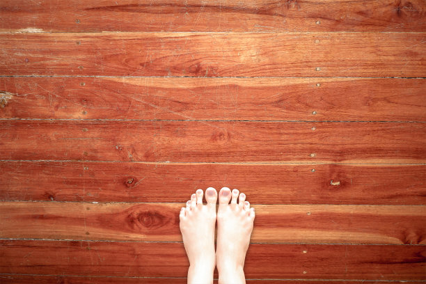 赤脚站在木地板背景，顶视图。女人光脚和腿在木头上的自拍。裁剪图像美丽的年轻女性身体腿与指甲在棕色足部和美甲。图片下载