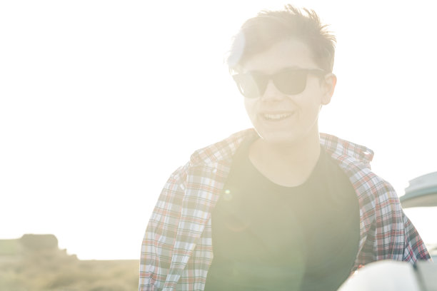 一个快乐的少年感觉快乐和微笑的肖像，明亮的天空在背景，土地太阳耀斑。户外的健康的生活方式。英俊的年轻人戴着黑色太阳镜享受假日户外图片下载