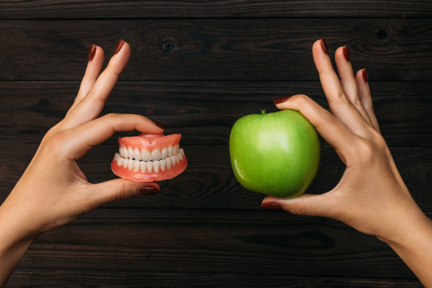 假牙和苹果在医生手里。假牙假牙对绿青苹果。假牙齿保健。牙科保健。美丽的牙齿。假肢。假牙图片下载