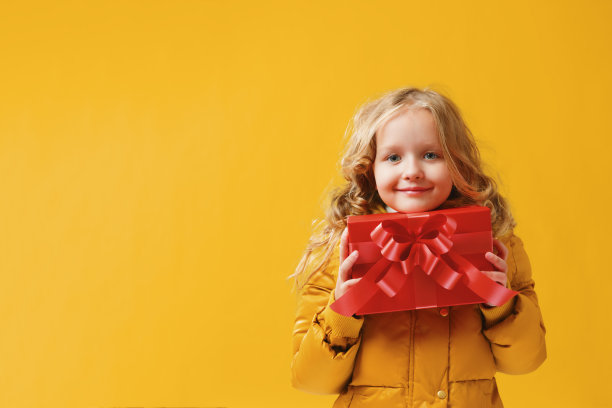 快乐的学龄前小女孩穿着一件冬季夹克，手里拿着一顶帽子图片下载