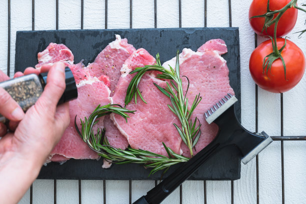 切菜板上的猪肉片，黑胡椒，迷迭香和西红柿。特写，俯视图。准备食物,配方图片下载
