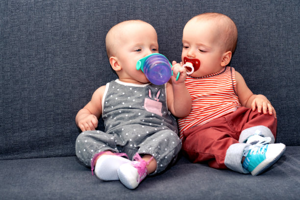 男孩和女孩直到今年都喝沙发上的瓶子里的水。家庭中双胞胎的概念。图片下载