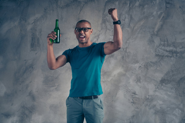 近距离照片令人惊奇的喊他他黑皮肤男人英俊的手臂握住的手提高玻璃啤酒酒饮料看足球赛比赛穿规格轻便的蓝色t恤孤立的灰色背景图片下载