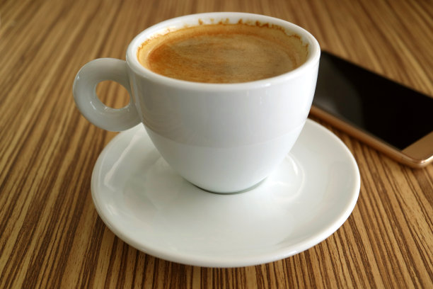 一杯热黑咖啡，背景是模糊的智能手机图片下载