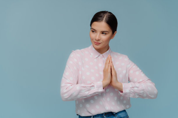 腰部向上的照片，可爱的女人压在一起，祈祷室内，焦点远离，穿着波尔卡点衬衫，有严肃的体贴的面部表情孤立在蓝色背景与标语的复制空间图片下载