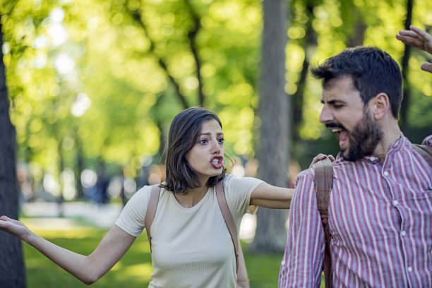 一对年轻夫妇在公园里吵架。一对情侣在一个有绿色背景的公园的户外严肃地交谈。夫妻争吵，对彼此不满意。图片下载