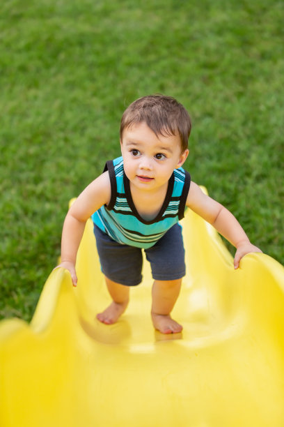 蹒跚学步的小男孩爬上户外黄色滑梯图片下载