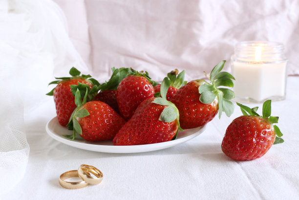 明亮的婚礼场景，配上新鲜草莓和婚戒的瓷盘，白色的背景。女性风格的库存照片。图片下载