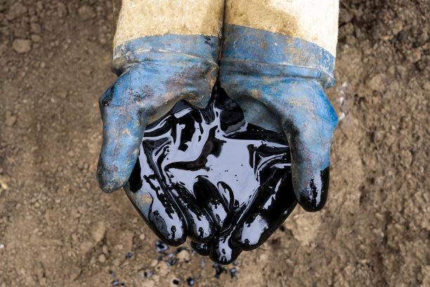 石油泄漏。很脏的手。在土壤背景上涂上黑色的油图片下载