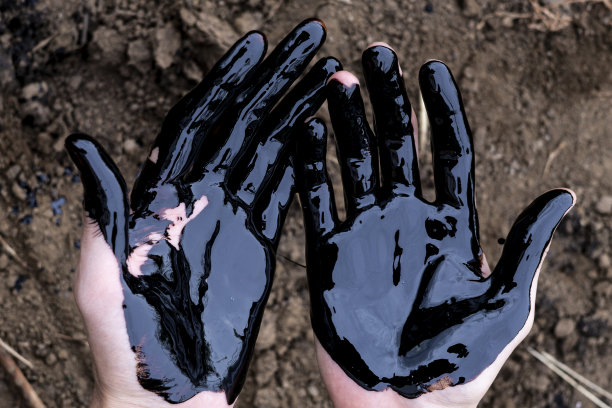 石油泄漏。很脏的手。在土壤背景上涂上黑色的油。图片下载