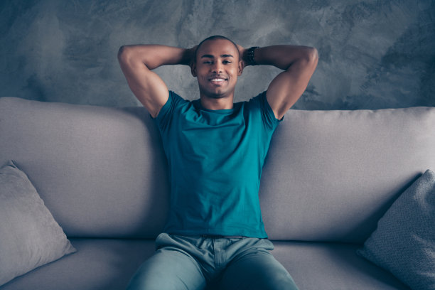 特写照片惊人的，时髦的，美丽的，他，他，他的黑皮肤，男子气概，英俊的，牵手，在后面的头，暂停，打破牙齿，清新，健康，穿蓝色的t恤裤子，坐舒适的沙发，房间，房子，室内图片下载