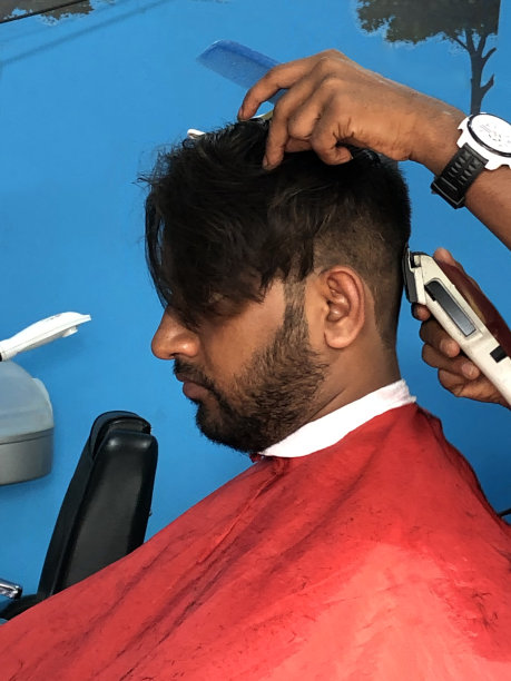 印度男子在发型师/男士理发店理发的形象，电动剃须刀/男性发型师用剪子修剪短的背部和两侧，在头发上梳和夹，修剪胡须，在衣服上修剪披肩图片下载