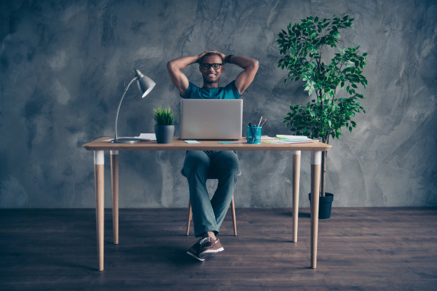 长身体尺寸照片惊人的他他他的英俊的样子笔记本桌子说话skype双手手臂后面的头绿色植物穿specs蓝色的t恤裤子坐椅子室内工作站办公室图片下载