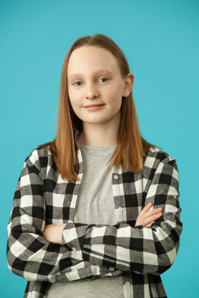 一个十几岁的金发女孩在一个蓝色背景格子衬衫肖像图片下载
