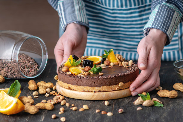 手装饰巧克力蛋糕、橘子和薄荷叶花生和坚果。健康的素食生甜点图片下载