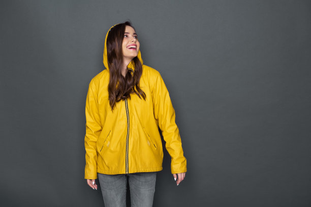 裁剪的照片，快乐的白人女孩穿着黄色雨衣在灰色的背景图片下载