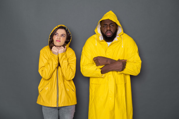 半长年轻的异族夫妇穿着黄色雨衣对抗灰色的背景图片下载