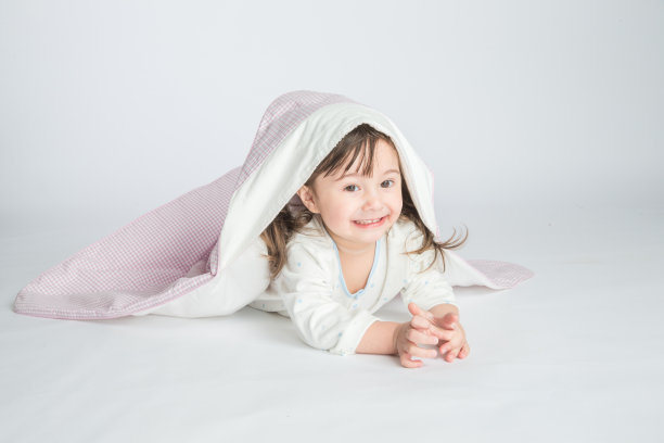 一个小女孩穿着家装，盖着婴儿毯，婴儿躺在地板上。水平的照片。浅灰色背景图片下载