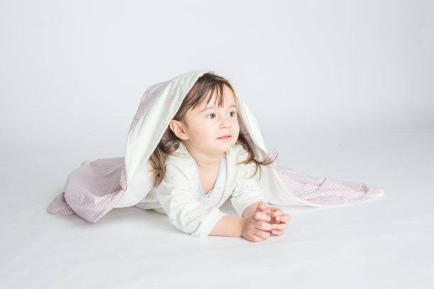 一个小女孩穿着家装，盖着婴儿毯，婴儿躺在地板上。水平的照片。浅灰色背景图片下载