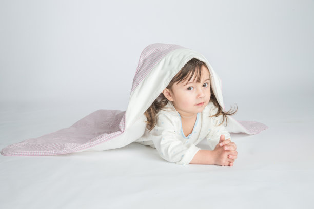 一个小女孩穿着家装，盖着婴儿毯，婴儿躺在地板上。水平的照片。浅灰色背景图片下载