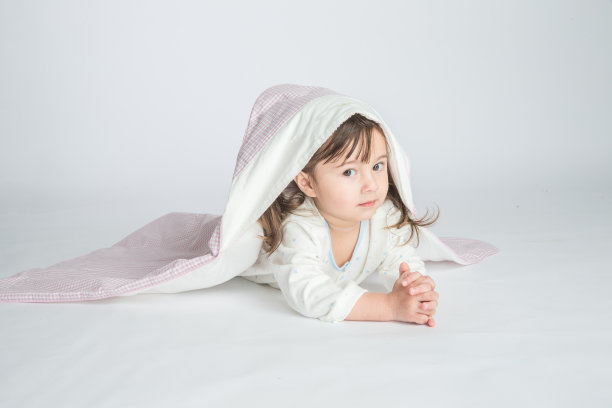 一个小女孩穿着家装，盖着婴儿毯，婴儿躺在地板上。水平的照片。浅灰色背景图片下载