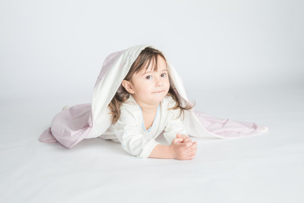 一个小女孩穿着家装，盖着婴儿毯，婴儿躺在地板上。水平的照片。浅灰色背景图片下载