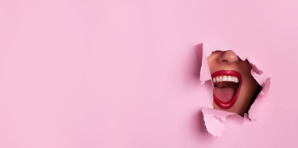 鲜红的嘴唇透过撕破的粉红色纸背景。惊讶的女孩,情绪。化妆师，美的概念。准备聚会。化妆品销售。美容院广告横幅，有文案空间图片下载