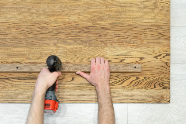 修理工手持电动螺丝刀工具进行修理的平放和头顶照片，固定在建造新的木质书桌或桌面上图片下载