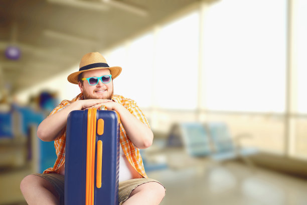 一个有趣的胖男人带着一个手提箱在机场度假。图片下载