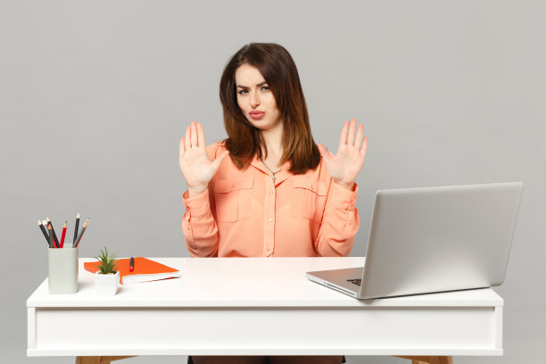 年轻迷惘的女人，穿着柔和的休闲衣服，显示手掌说，没有工作在白色的桌子上，电脑笔记本电脑孤立在灰色的背景。成就商业事业生活理念。模拟拷贝空间。图片下载