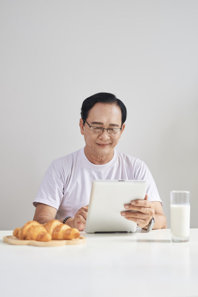 老人喝牛奶，在他的数字平板电脑上阅读新闻，而不是报纸图片下载