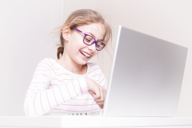 快乐微笑的小女孩(孩子)使用笔记本电脑图片下载