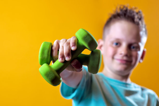 一个穿着亮t恤黄色背景上有哑铃的男孩图片下载