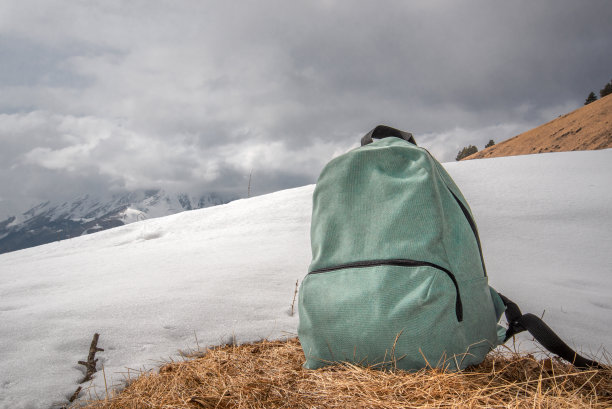 背包站在干燥的草地上，旁边是雪图片下载